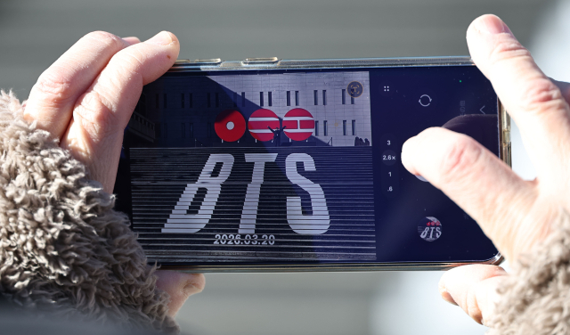 지난달 22일 서울 종로구 세종문화회관 계단에서 일본인 관광객들이 오는 3월 3년 9개월 만에 '완전체'로 돌아오는 그룹 방탄소년단(BTS)의 컴백을 알리는 홍보물을 기념촬영하고 있다. 연합뉴스